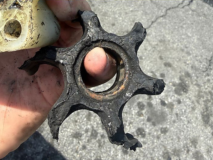 A worn outboard water pump impeller held in a hand, several of its rubber vanes broken off