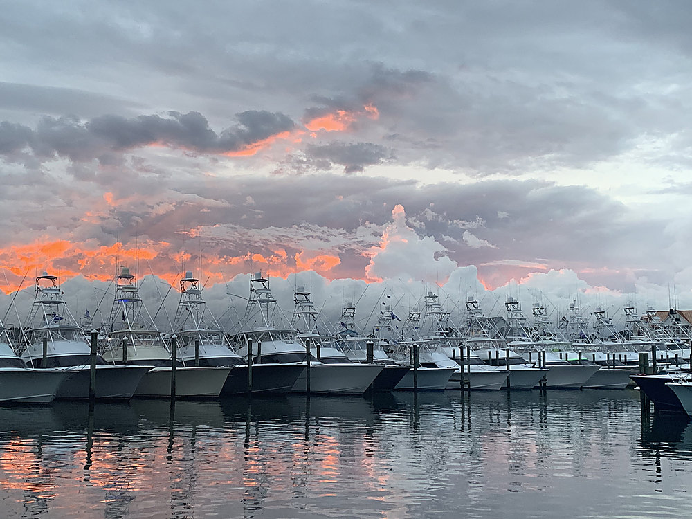 A row of sportfishing boats in their slips under a sunset sky, reflected in the water