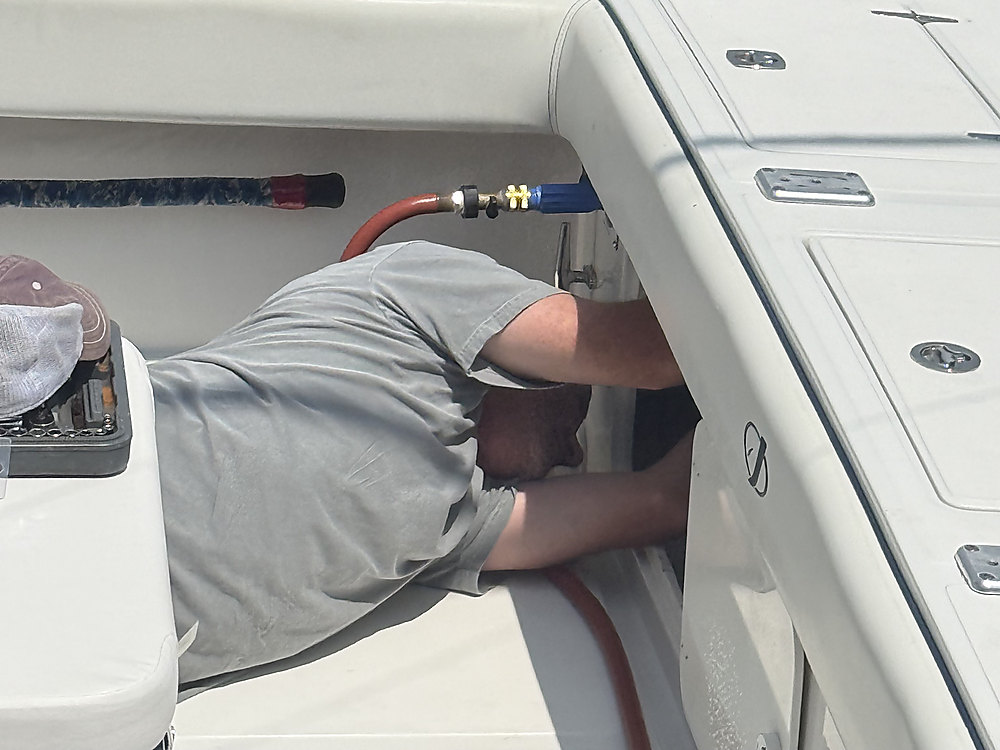 A technician lying in the cockpit, running a hose line under the gunwale