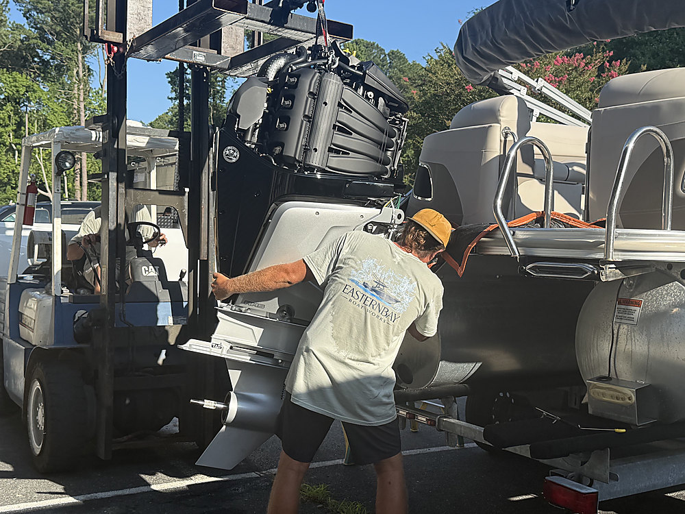A technician guiding the new Mercury outboard onto the transom
