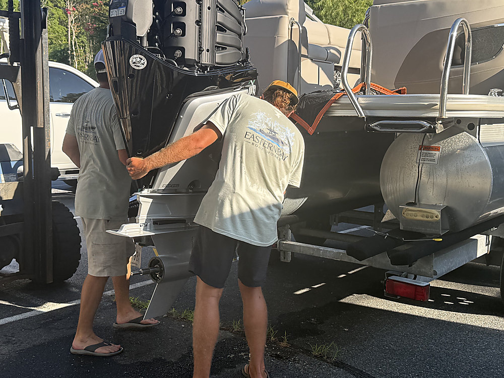 Two technicians setting the new Mercury outboard onto the boat's transom